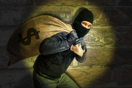 Photo illustration of a hooded bank robber making off with a big bag of cash.