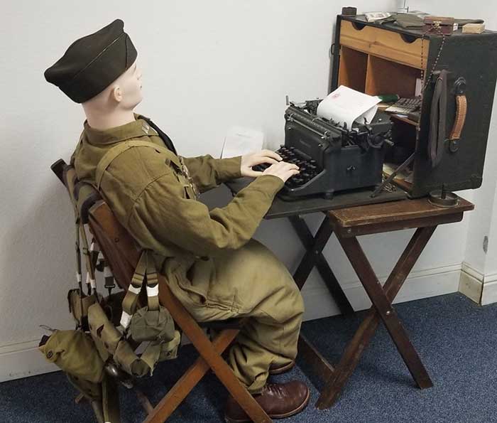Mannequin dressed as soldier, seated at typewriter.