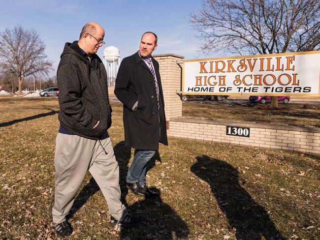 Two gentleman walking in front of the Kirksville High School discussing Kidney donation at the Home of The Tigers