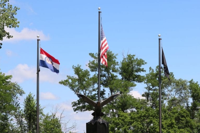 Flags and eagle statue against a treeline