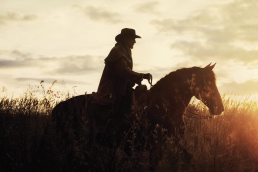 Person riding a horse in the sunset with old western garb